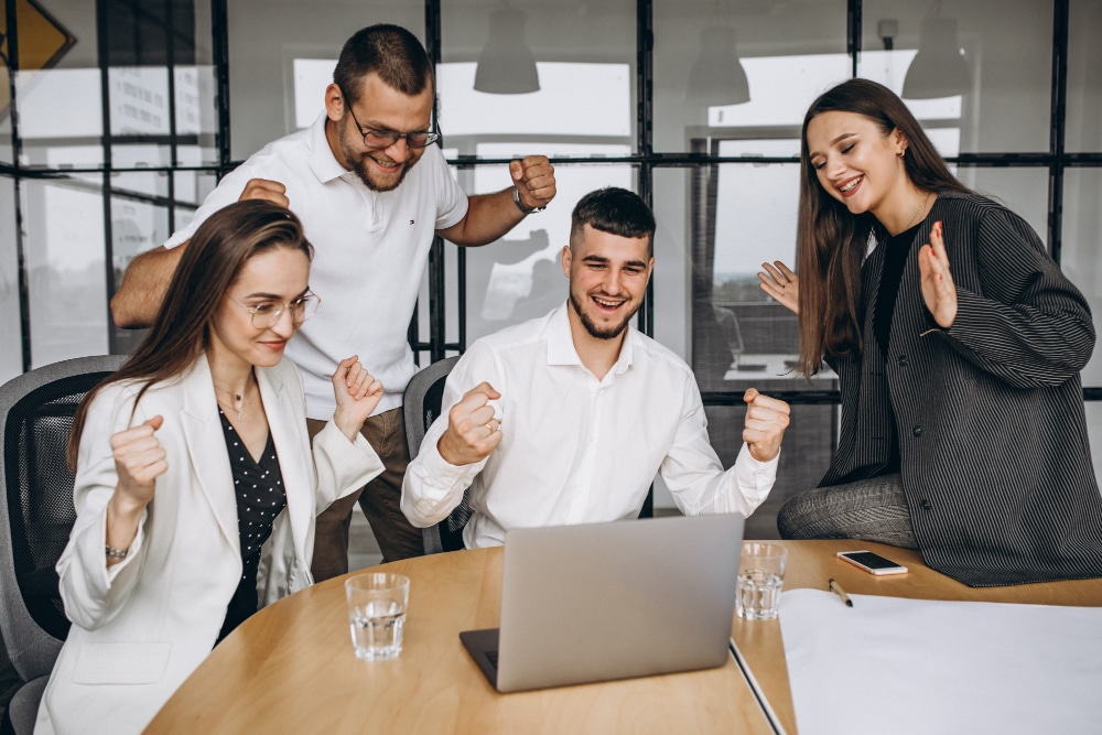 Happy team celebrating around a laptop, showing employee re-engagement.
