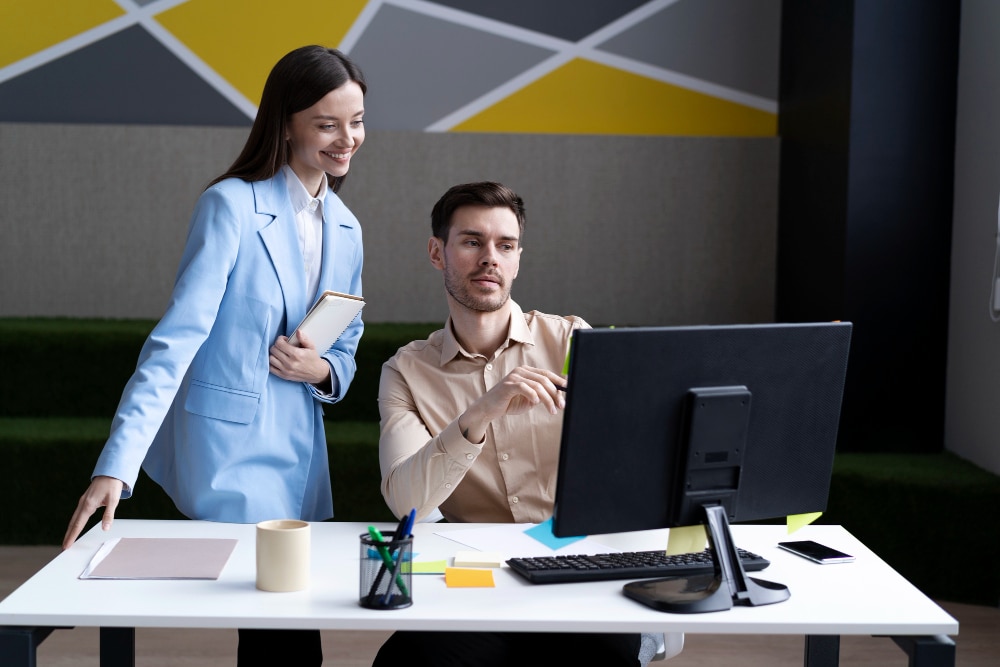 Two colleagues reviewing performance data on a computer, representing different types of performance reviews in a modern workplace setting.