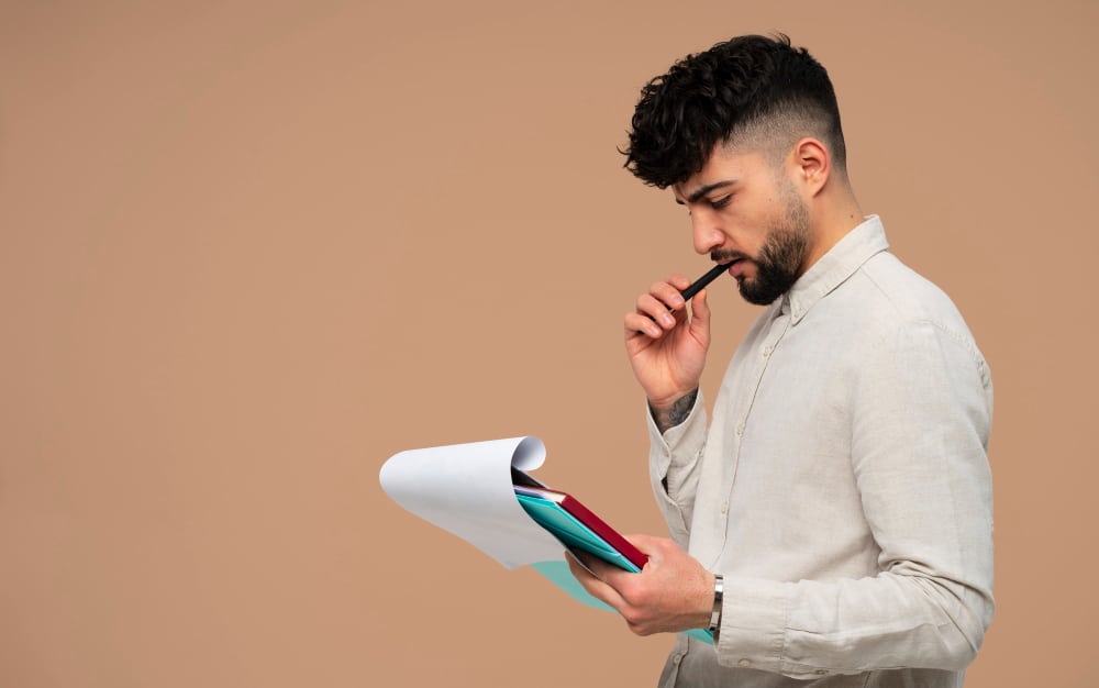 A man thoughtfully reviewing documents and holding a pen, representing the concept of self-assessment.

