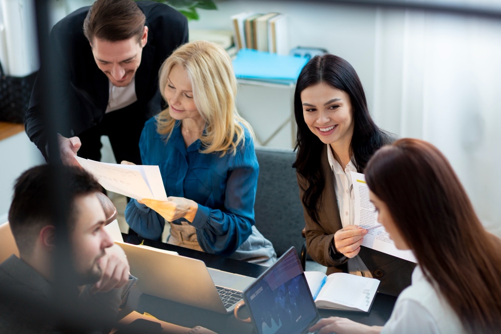 Team of professionals smiling and collaborating around a table, showing an engaged workforce.
