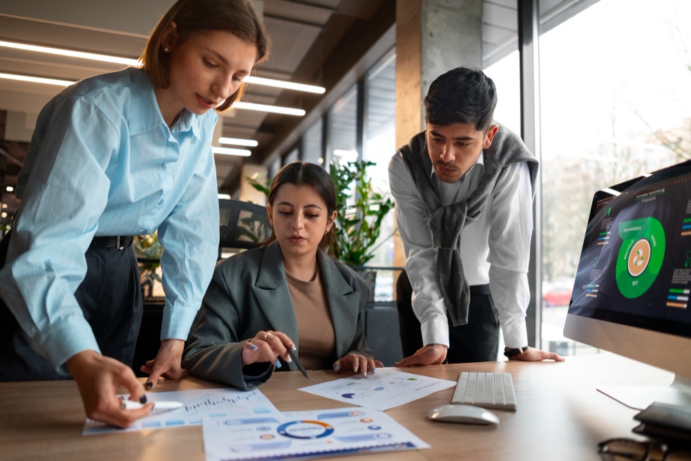 Team of professionals analyzing business data and charts together in a modern office setting with a digital dashboard on screen