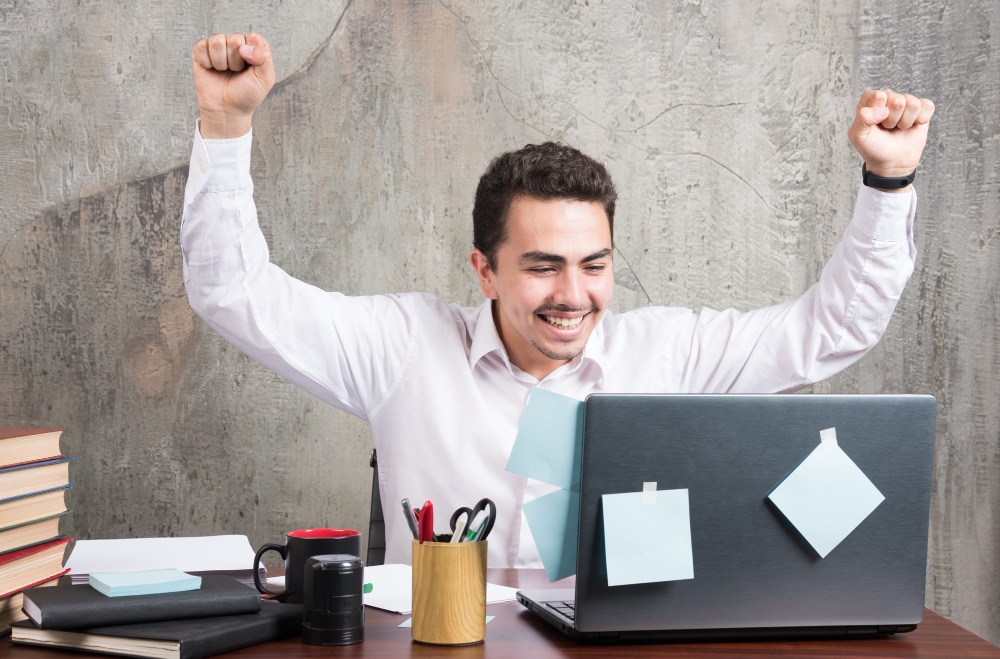Person at a desk celebrating with raised fists and a smile.