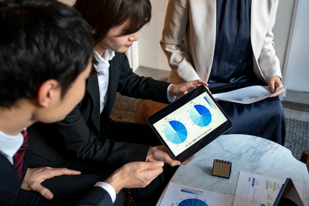Business professionals reviewing pie chart data on a tablet during a meeting.