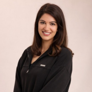 Smiling woman with long dark hair wearing a black quarter-zip top, photographed against a plain neutral background.