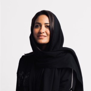 Smiling woman wearing a black hijab and abaya, photographed against a plain white background.